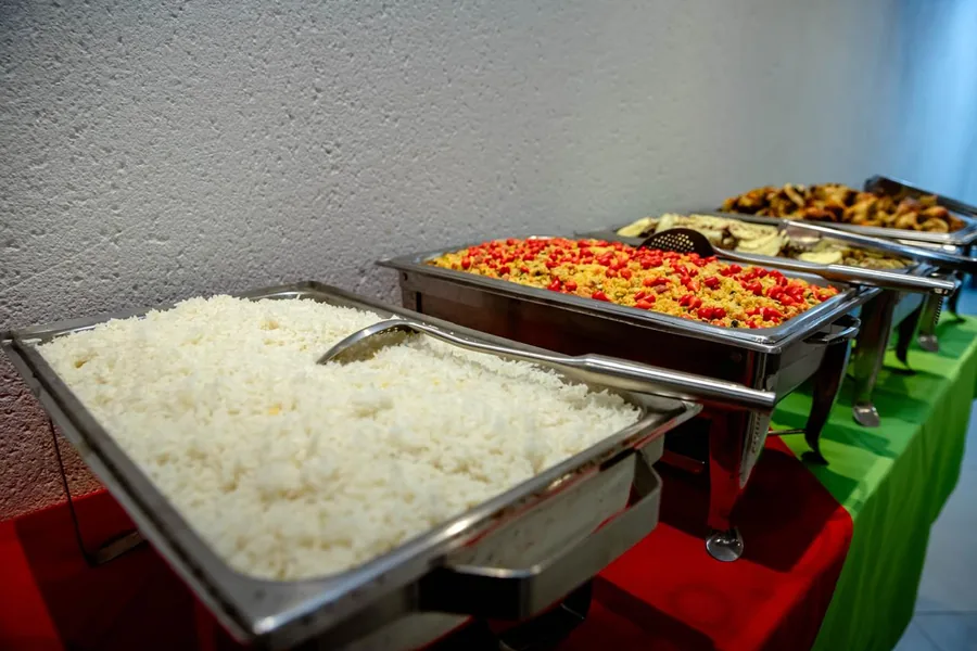 Arroz, farofa colorida e frango assado nos rechauds do buffet de uma festa no 3:16